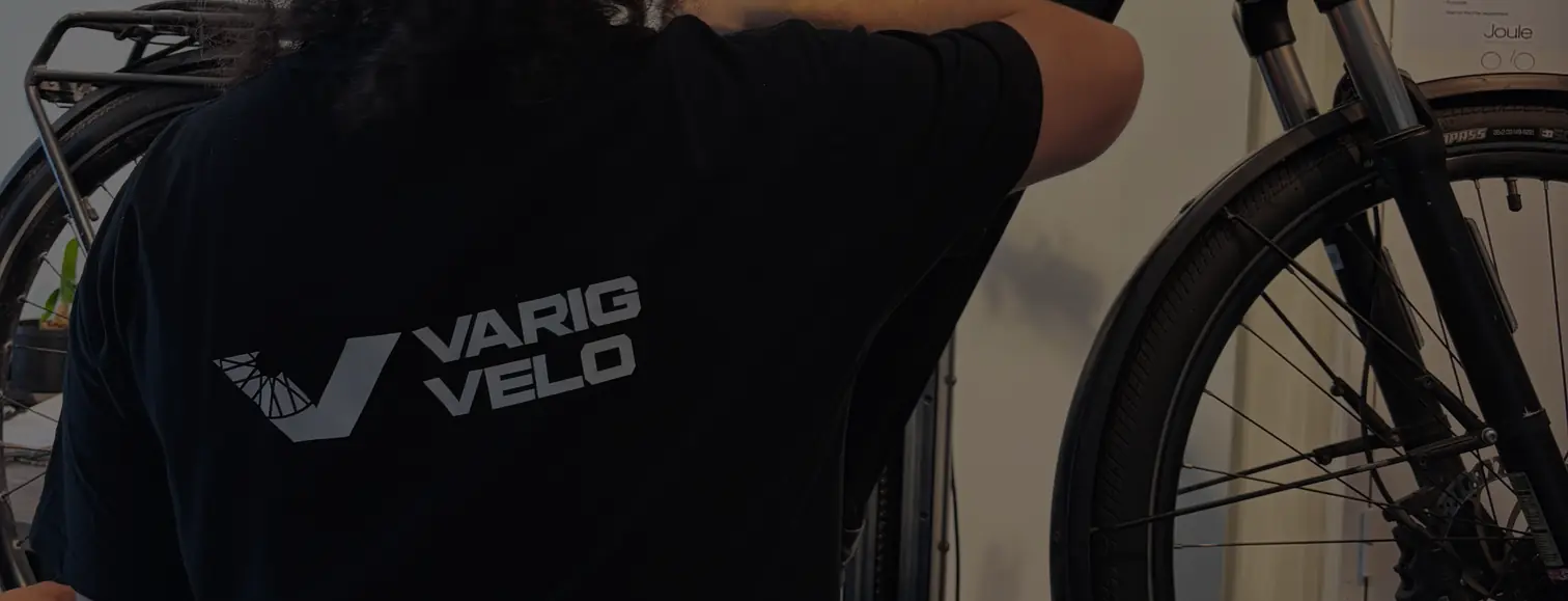 Mekaniker hos Varig Velo sett bakfra, med logoen på ryggen av t-skjorten, i arbeid med en sykkel.